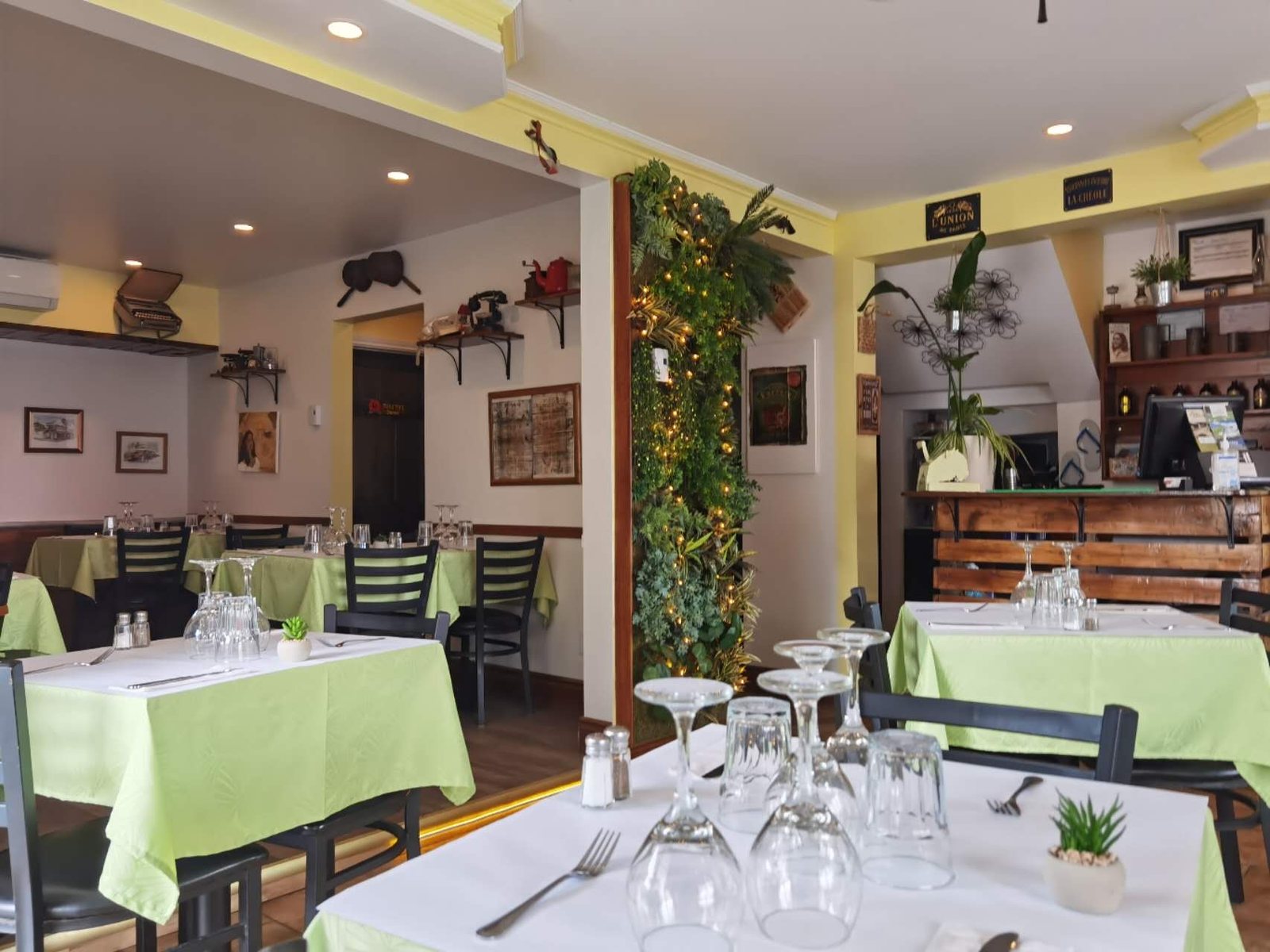 La salle à manger de L'Hibiscus : nappes vert tendre, couverts dressés et une colonne de verdure illuminée
